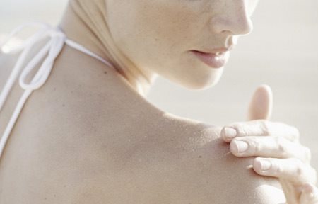 Žena aplikující krém na pravé rameno